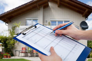 A home inspector holds a clipboard with an inspection checklist in front of a house.